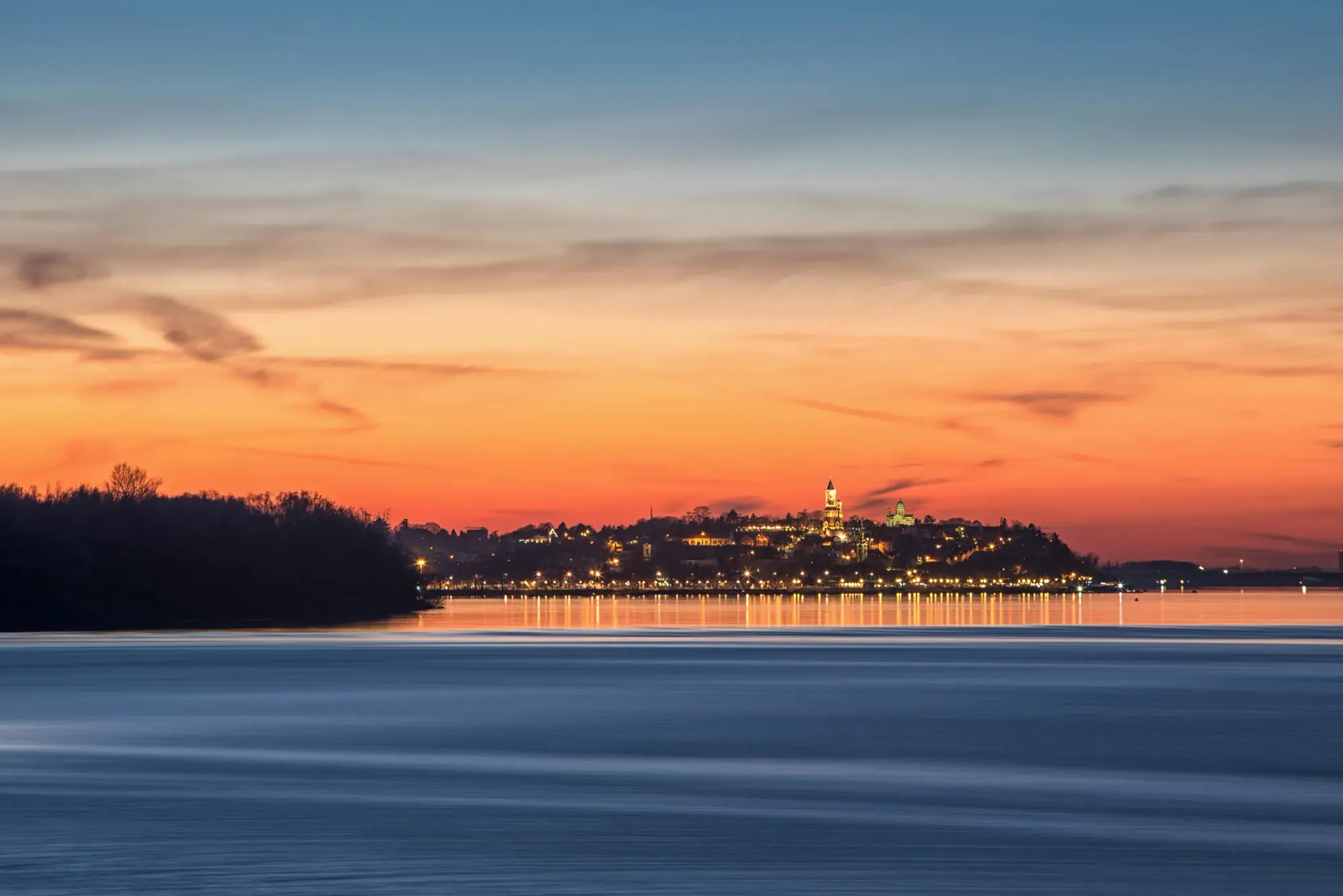 Belgrade city on top of a hill, seen from across a lake, at sunset.