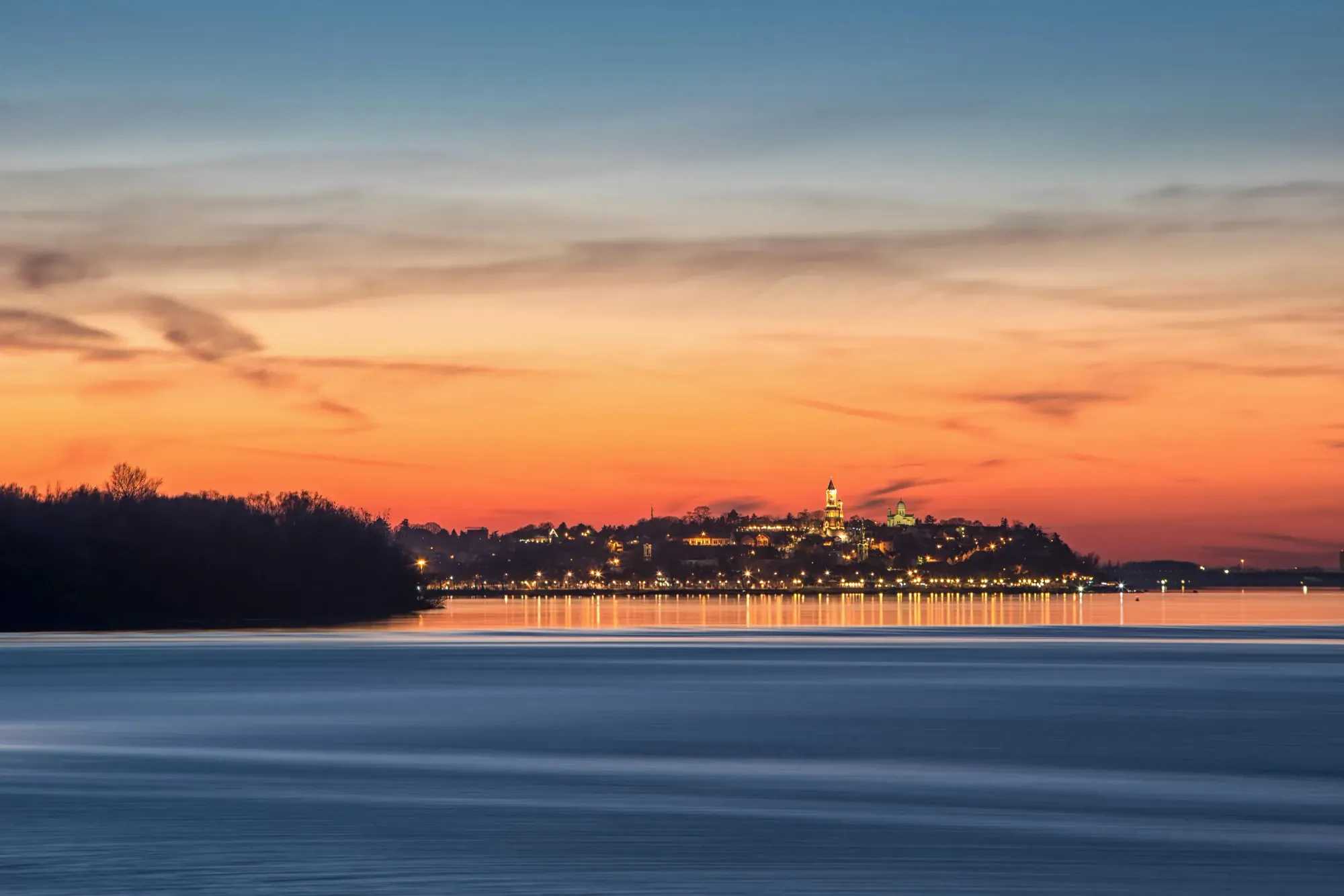 Belgrade city on top of a hill, seen from across a lake, at sunset.