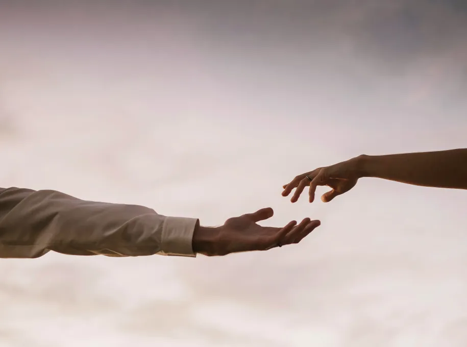 Close-up of a man reaching out to a woman's hand, with a sky background.