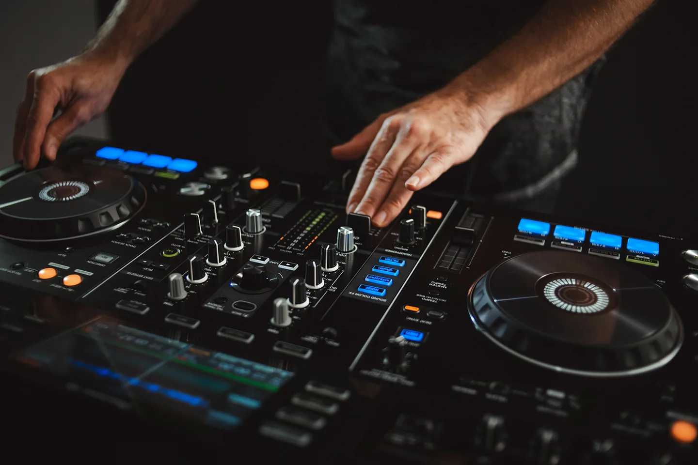 A close-up shot of the hands of an expert DJ at work, engaging with their controller and mixer in front of them.