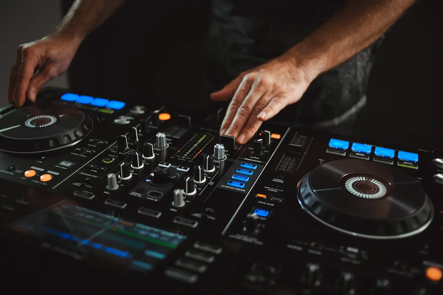 A close-up shot of the hands of an expert DJ at work, engaging with their controller and mixer in front of them.