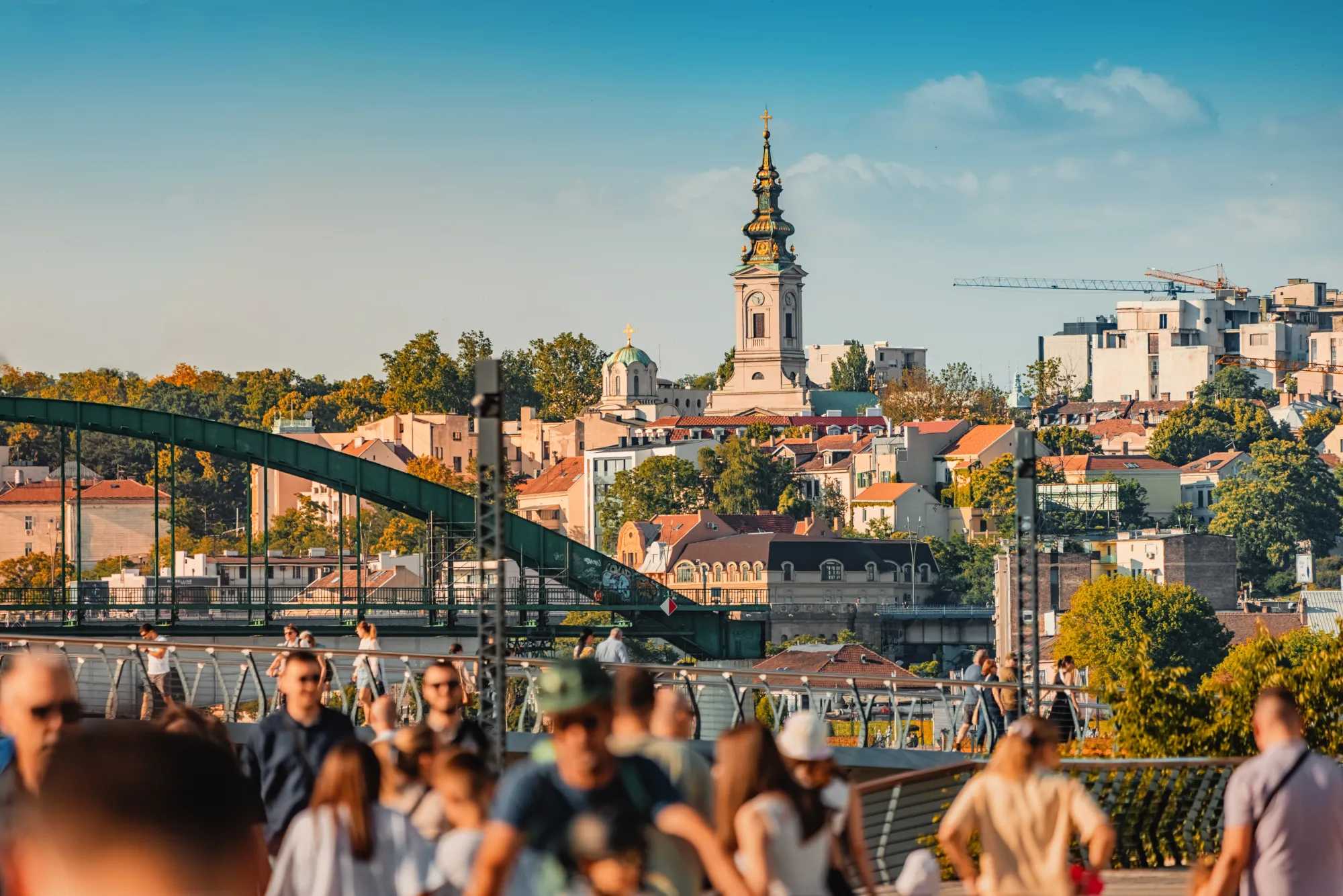 The old town of Belgrade above the Sava river, with a cathedral bell tower and people walking in the foreground.