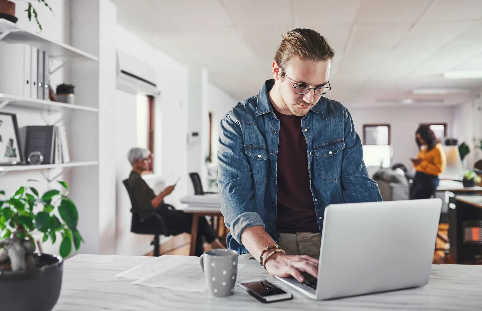 A software engineer working at a laptop in an open-plan office.