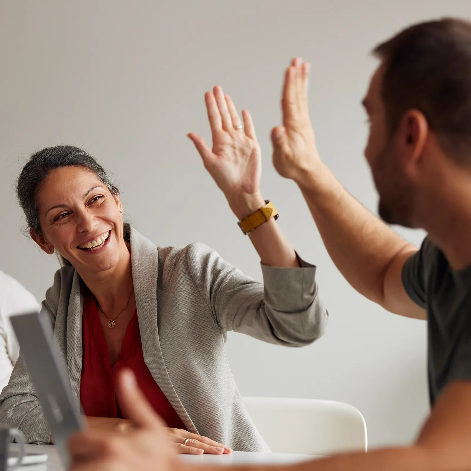 Two business people high-fiving at an office table, laughing and smiling in the foreground.