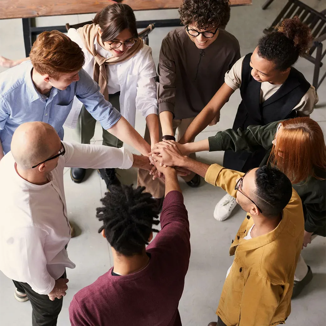 A diverse group of people standing in an office, holding hands and forming circle.