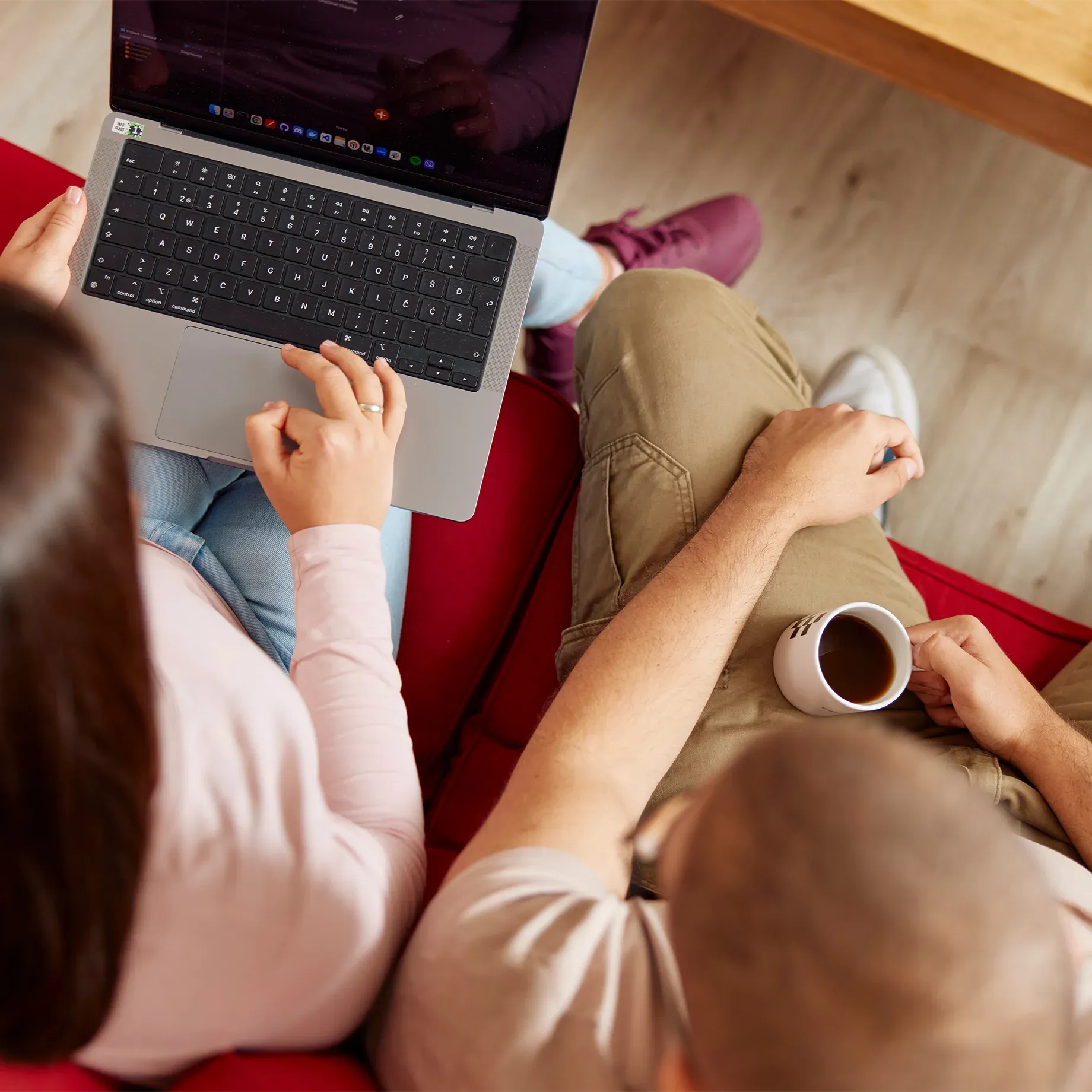 A man and woman sitting on the sofa with their laptop, top view of them holding coffee mugs while watching on screen.