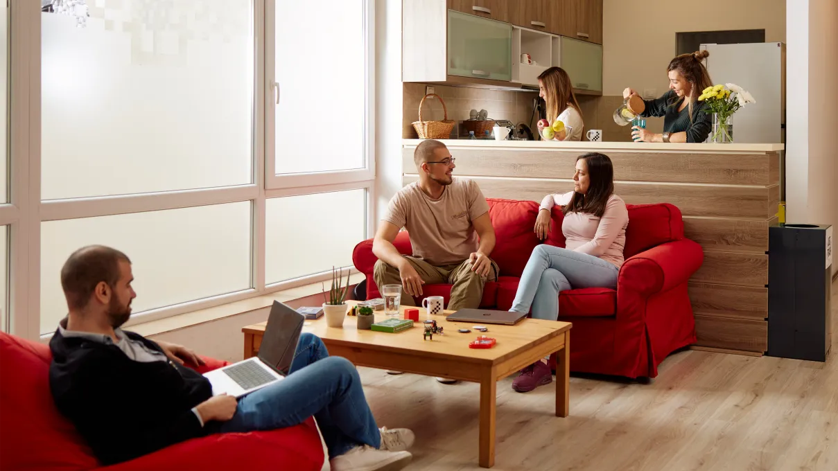 Group of people sitting on red sofas in the office, a wooden table with coffee mugs and laptops in front.