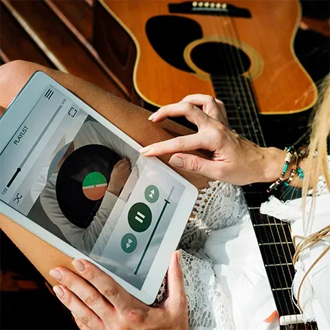 A close-up photo of an iPad with green buttons and a music player on the screen, held by two hands.