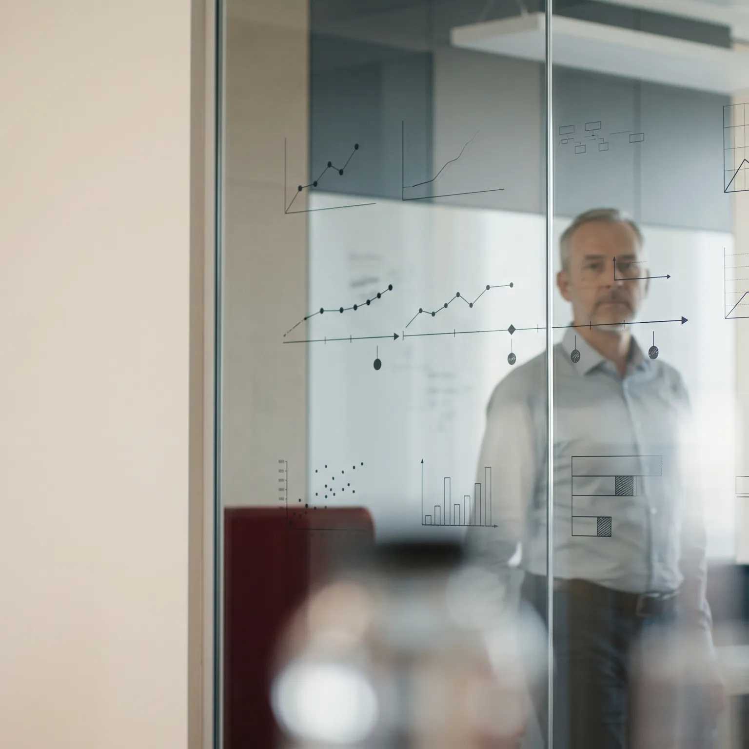 A man standing behind a glass wall covered in hand-drawn charts.