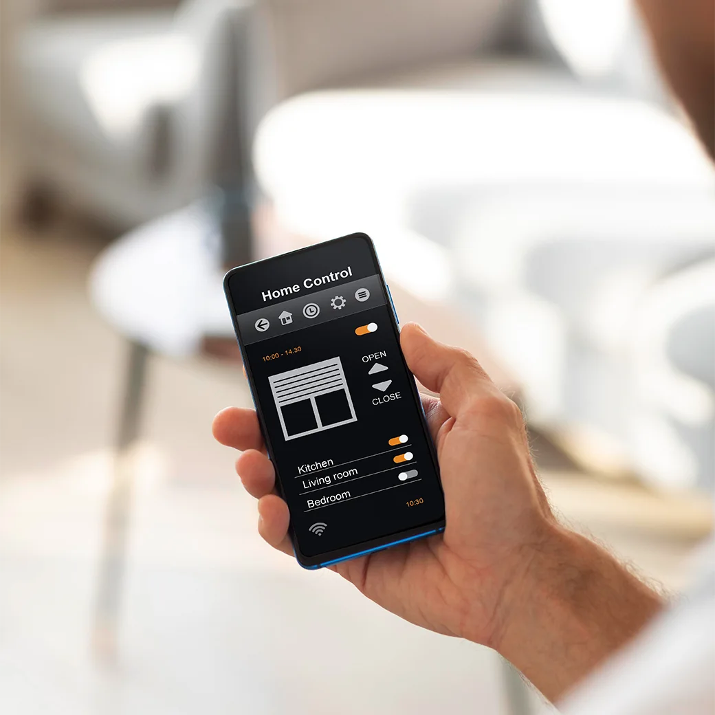 An over-the-shoulder shot of an individual holding and interacting with their phone, displaying the "Home Control" app interface on screen in a modern living room setting.