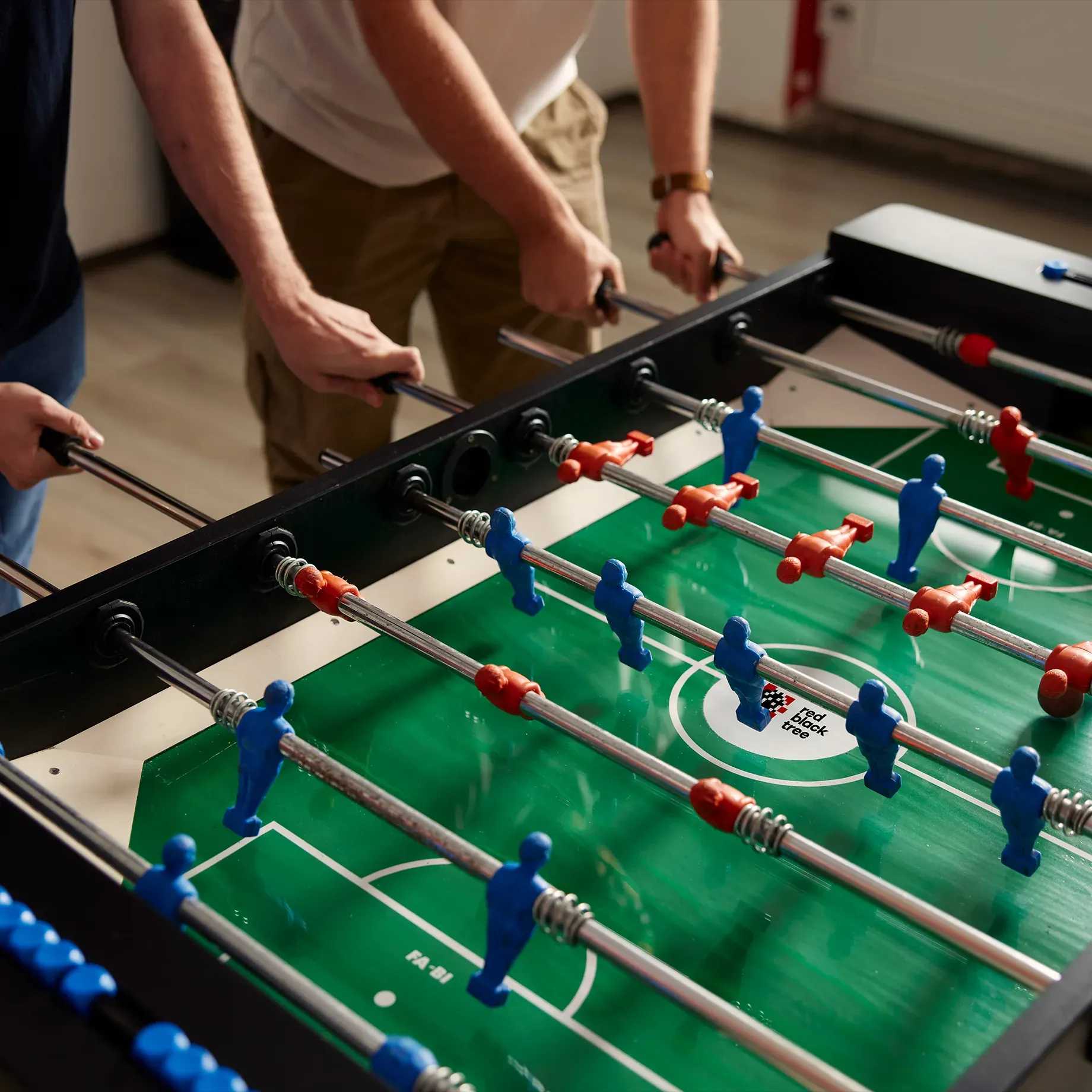 Foosball table, close up of people playing game in an office environment
