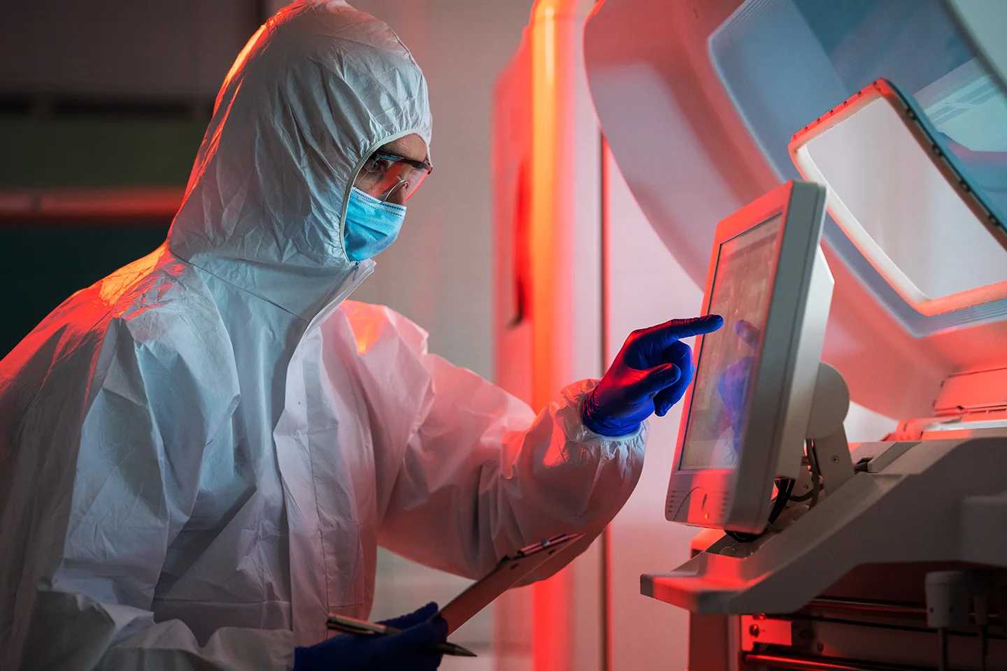 A scientist in protective gear is using an interactive computer screen.